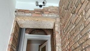Eine enge Treppe mit einer Backsteinwand an einer Seite und einer weißen Wand an der anderen, die zu einem Raum mit einer roten Matte auf dem Boden führt.