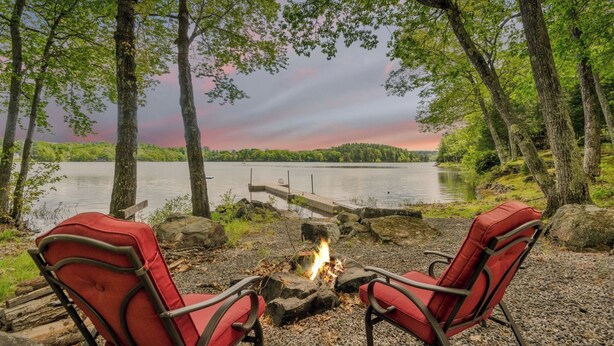 Un cadre idyllique au bord d’un lac, avec deux chaises rouges disposées face à un feu de camp, entourées d’arbres et offrant une vue sur le lac.