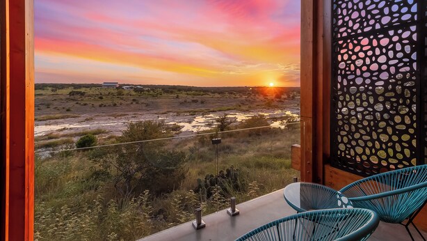 Un balcón con vistas a un atardecer sobre un paisaje, con baranda de madera y un panel decorativo.