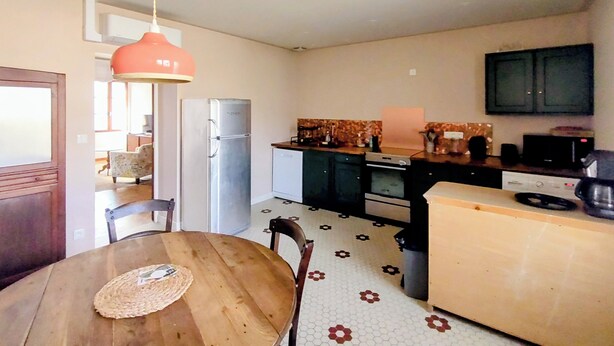 A compact kitchen with a refrigerator, microwave, and stove. There is a dining table with chairs and a hanging light fixture. - Village house with garden  (Monségur)