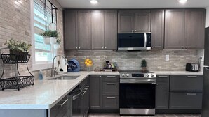 Une cuisine moderne avec des meubles de couleur sombre, un réfrigérateur en acier inoxydable, un four à micro-ondes et une cuisinière à gaz.