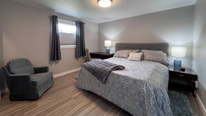 Une chambre à coucher avec un lit, une chaise, une table de chevet, une lampe et une fenêtre avec des rideaux.