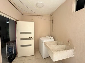 Une buanderie équipée d’un lave-linge, d’un évier en béton et d’une porte dotée d’une poignée en métal.