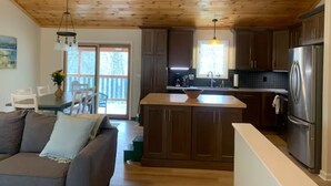 A modern kitchen with wooden cabinets, a stainless steel refrigerator, and a dining area with a table and chairs. - Howard's Creek Hideaway - Cozy mountain home close to downtown Boone & App State (Boone)