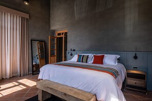 A bedroom with a large bed, a wooden bench, a nightstand, a wardrobe, and a mirror. - Veinticinco20h (Querétaro)