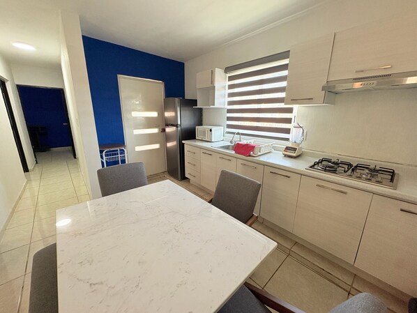 Una cocina moderna con encimera de mármol, electrodomésticos de acero inoxidable y una ventana con persianas.