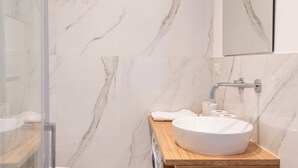 Un baño con pared de mármol, encimera de madera, lavabo blanco y espejo sobre el lavabo.