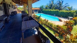 A covered outdoor area with wicker furniture and a pool. - Pousada Sol Nascente (Beberibe)