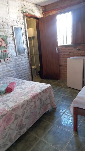 A small, compact room with a bed, a table, a refrigerator, and a shower area. - Pousada Sol Nascente (Beberibe)