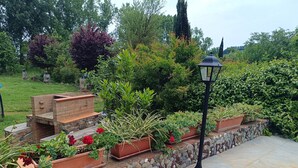 Ein Garten mit Grillplatz aus Ziegelsteinen, Steinmauern und verschiedenen Topfpflanzen.