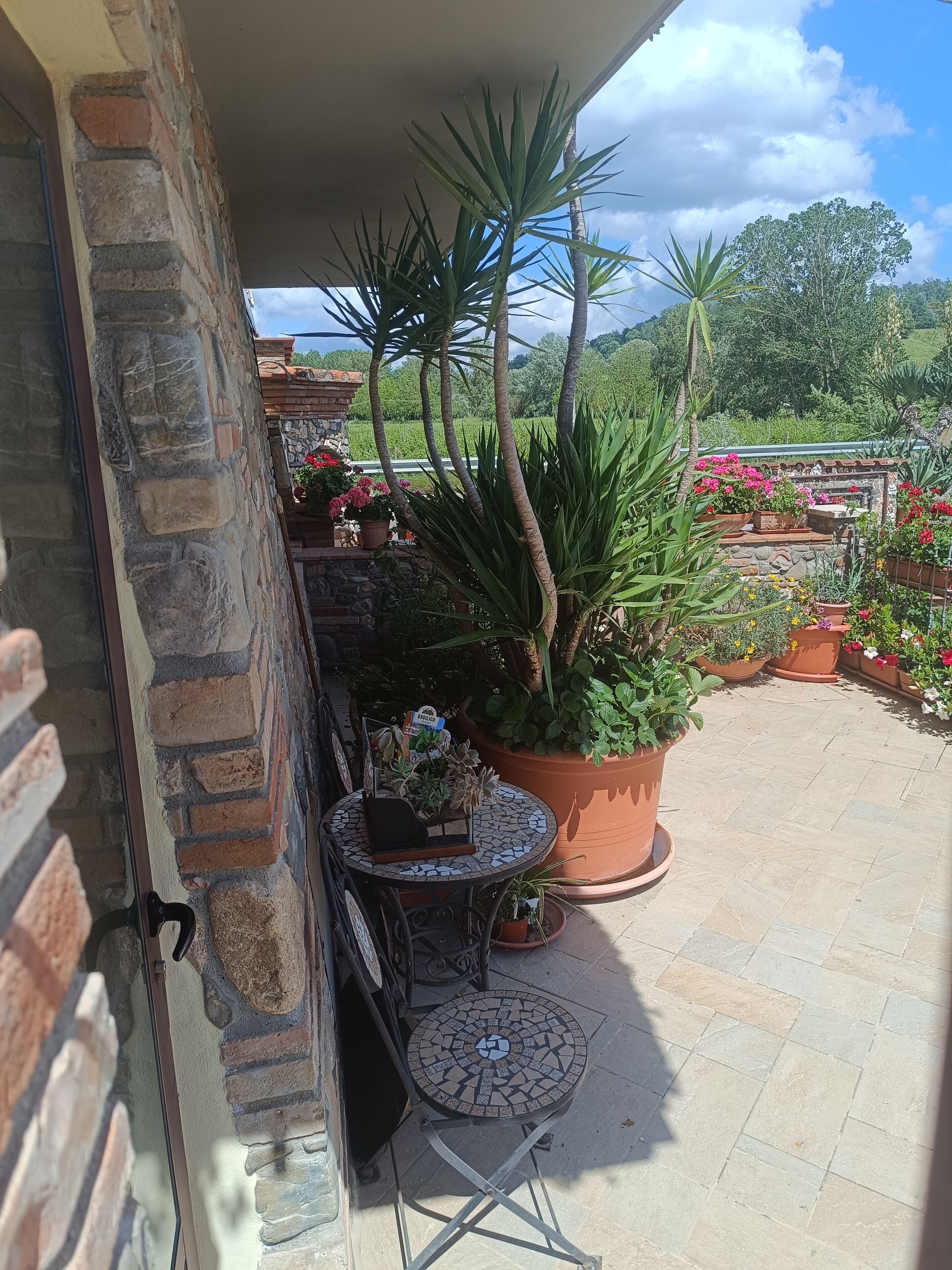A patio with a stone wall, a tiled table, and potted plants.
