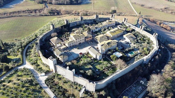 Eine Vogelperspektive auf eine befestigte Stadt mit einem zentralen Innenhof, umgeben von Steinmauern und Gebäuden im traditionellen Stil.