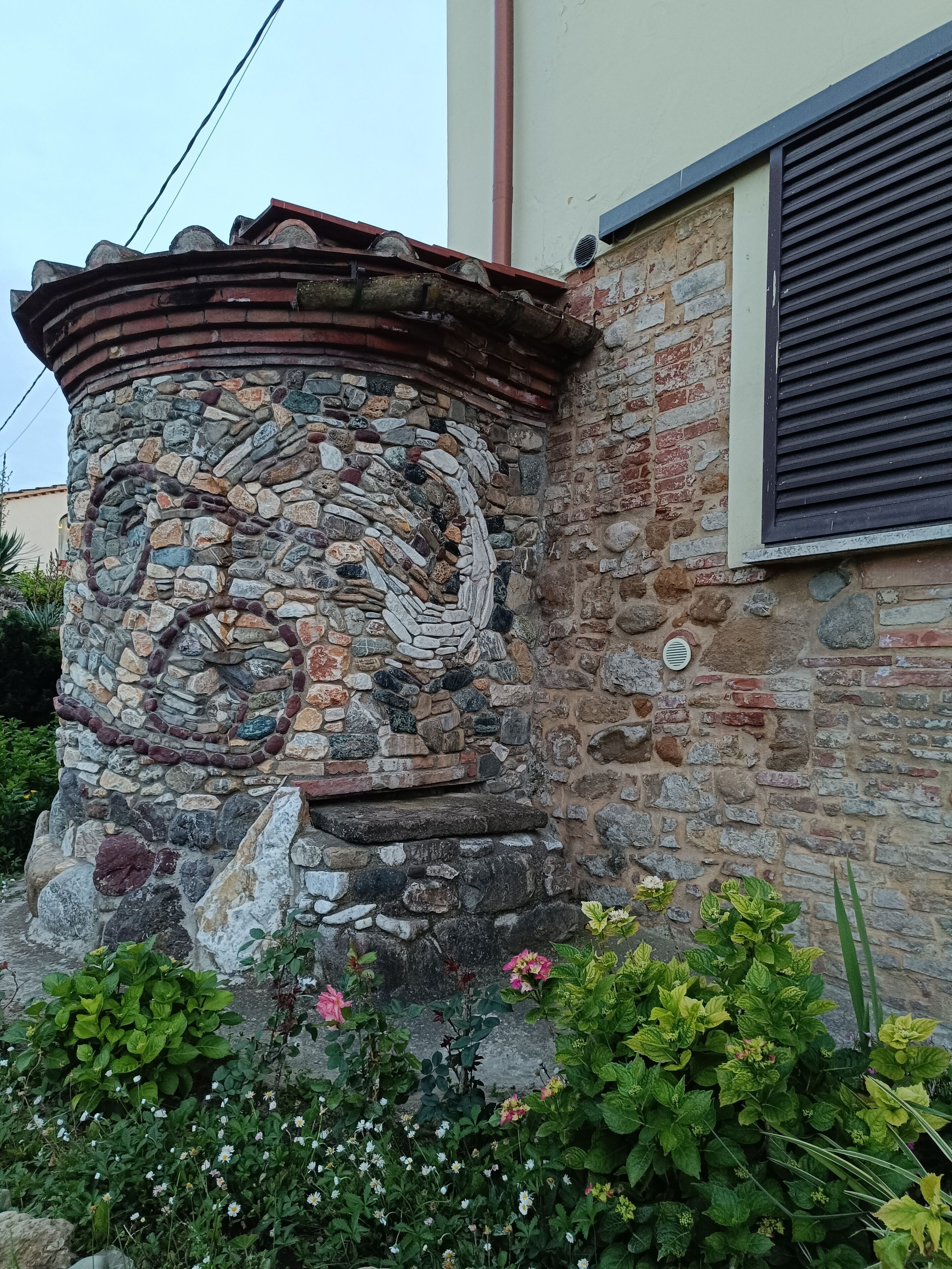 Un pilier en pierre orné d’un motif en spirale, un mur en briques et une fenêtre avec des stores.
