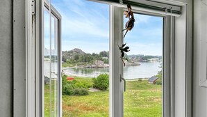 A view through a window with a landscape including a lake, greenery, and buildings in the background. - Cozy home in Hellvik with WiFi (Hellvik)