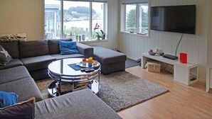 A modern living room with a grey sectional sofa, a round coffee table, and a flat-screen TV mounted on the wall. - Cozy home in Hellvik with WiFi (Hellvik)