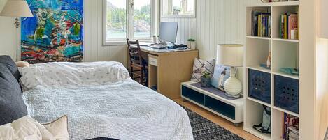 Un dormitorio con cama, escritorio, estantería y un cuadro grande.