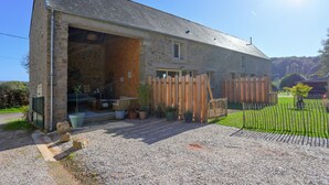 A stone building with a large open garage door, a gravel driveway, and a wooden fence. - 3 bedroom lovely home in La Pernelle (La Pernelle)