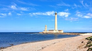 A coastal lighthouse with a tall, slender tower and a shorter structure nearby, situated on a pebbly beach with the ocean in the background. - 3 bedroom lovely home in La Pernelle (La Pernelle)