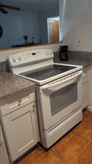 A kitchen with a stove, oven, granite countertop, and white cabinetry.