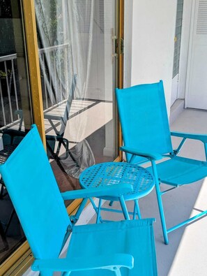 Eine Glastür führt zu einem Balkon mit zwei blauen Stühlen und einem kleinen runden Tisch.