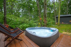 Ein Whirlpool auf einer Holzterrasse, umgeben von Bäumen, mit einem Stuhl und einem Blumentopf in der Nähe.