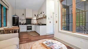 Een moderne keuken met witte kasten, een eethoek met een houten tafel en stoelen, en een groot raam met uitzicht op de omgeving.