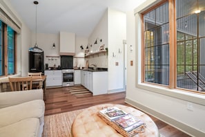 A modern kitchen with white cabinets, a central island, and a dining area with a sofa and table. - Evermore Cottage | Hocking Hills, Couples Retreat (Creola)