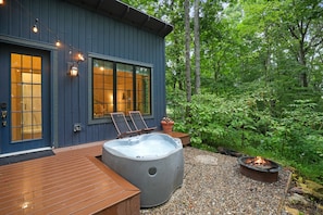 A wooden deck with a hot tub and a fire pit, surrounded by lush greenery. - Evermore Cottage | Hocking Hills, Couples Retreat (Creola)