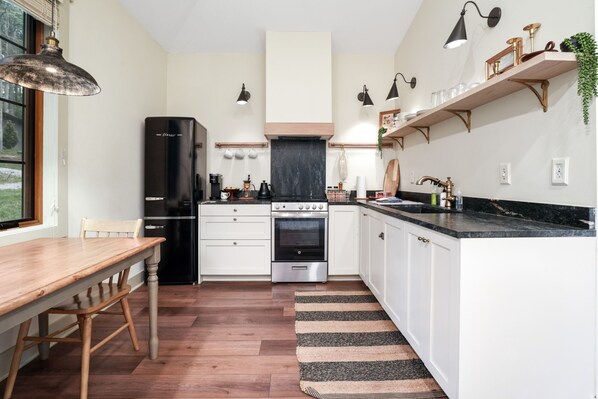 A modern kitchen with white cabinets, a black refrigerator, a stainless steel oven, and a wooden dining table.