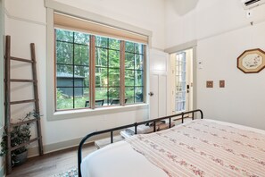 A bedroom with a large window, a bed, a ladder, and a potted plant.