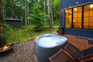 A hot tub on a wooden deck with a view of a house and forest.