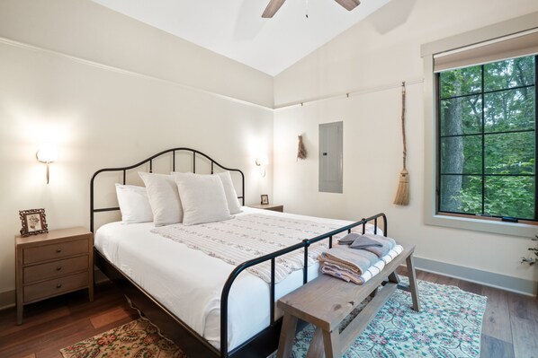 A bedroom with a bed, bedside tables, a window with a view of trees, and a ceiling fan.