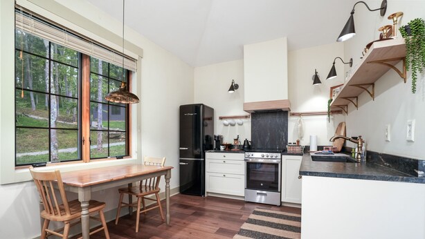 Een keuken met een eettafel, stoelen, een koelkast, oven en een raam met zonwering.