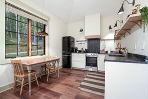 A kitchen with a dining table, chairs, a refrigerator, oven, and a window with blinds.