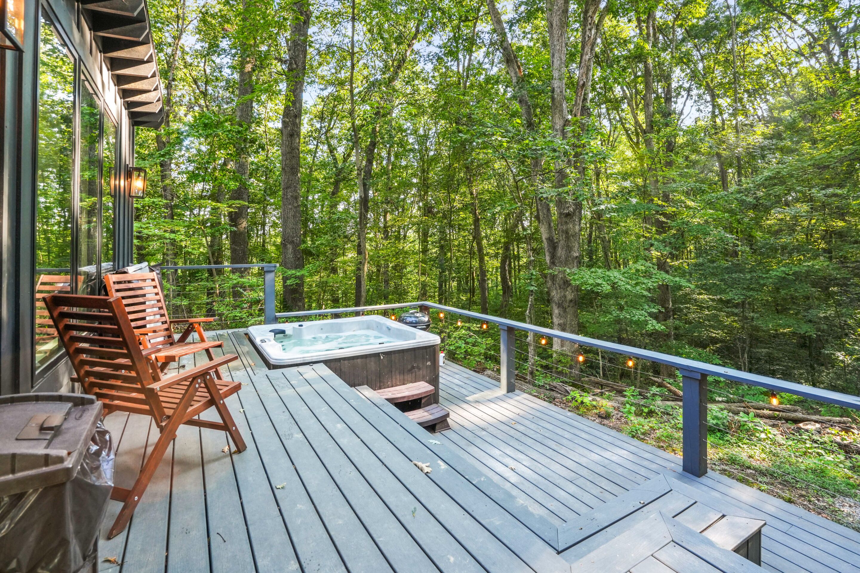 A wooden deck with outdoor furniture, a hot tub, and a view of a forest.
