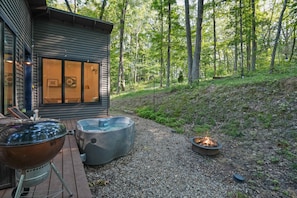 Una terraza de madera con una parrilla, un jacuzzi y un pozo de fuego.