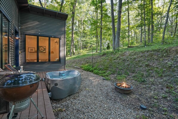 A wooden deck with a barbecue grill, a hot tub, and a fire pit.