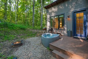 A wooden deck with a hot tub, outdoor seating, and a fire pit.