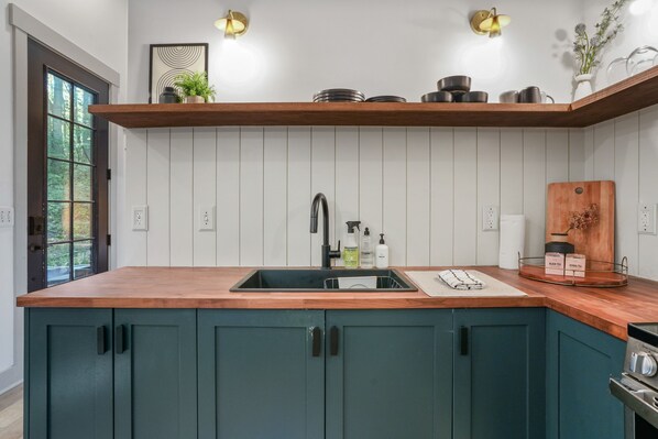 Cocina con encimera de madera, pileta y muebles de color turquesa. Cuenta con dos luces empotradas y ventana con vista a la vegetación.