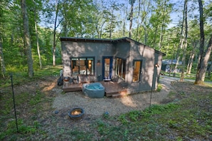 Una cabaña con terraza, jacuzzi y un hogar en un área boscosa.