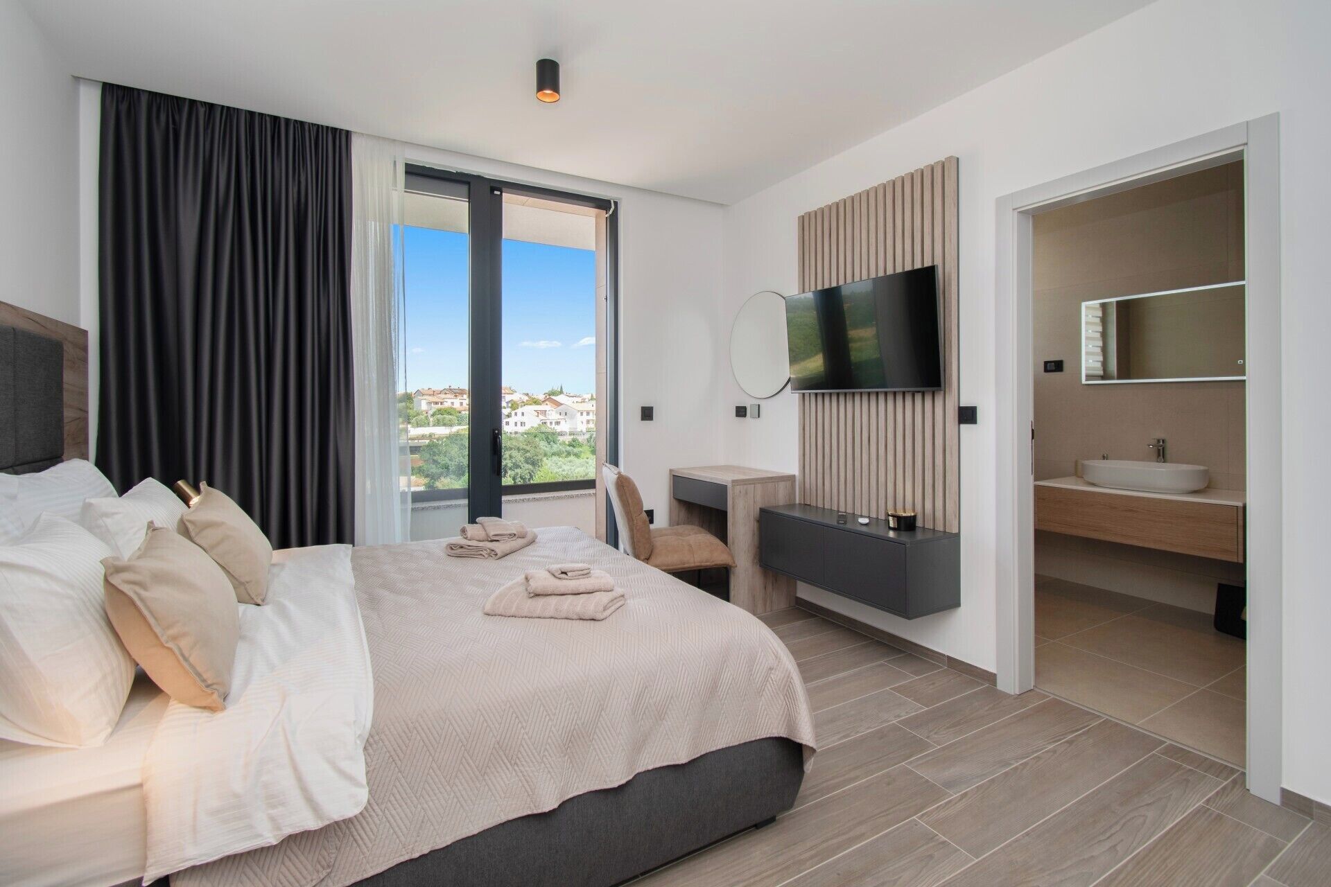 A modern hotel room with a large bed, a TV, a desk, and a bathroom.