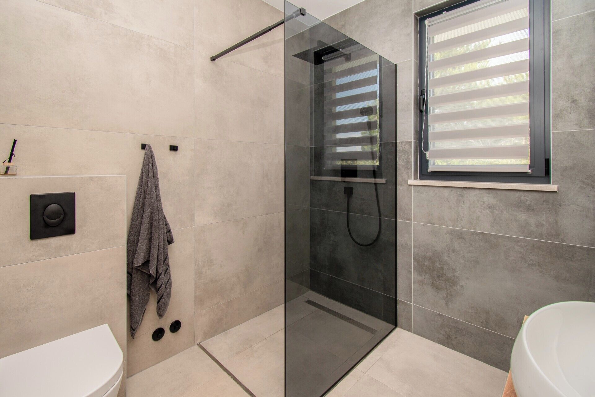Une salle de bain moderne avec une douche à parois de verre, des toilettes et une fenêtre équipée de stores.