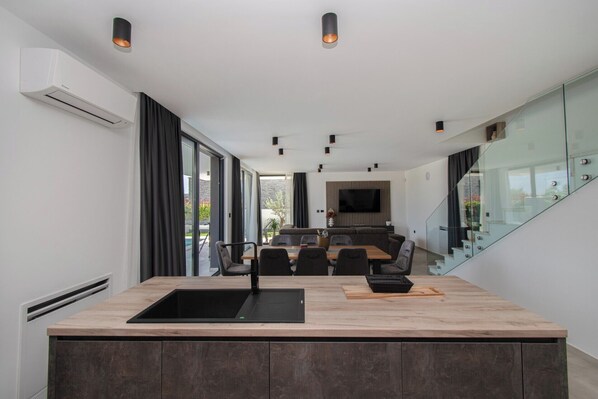 A modern kitchen with a central island, a dining area with a sofa, and a TV mounted on the wall.