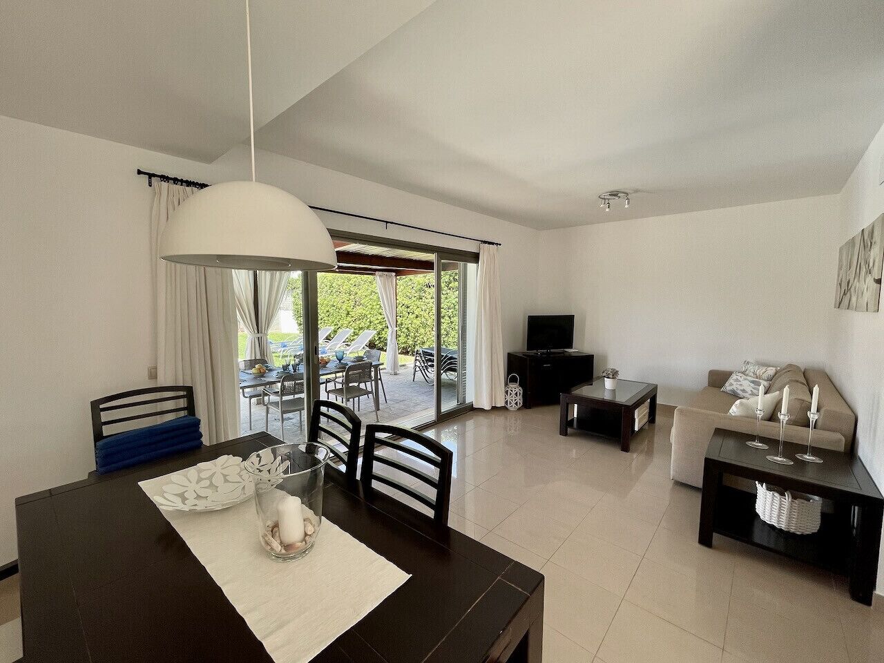 A modern living room with a dining area, a sofa, a TV, and a balcony with outdoor furniture.