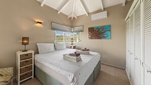 A bedroom with a large bed, a nightstand, a lamp, a window with blinds, a painting, and a wardrobe. - Jan Thiel Jewel (Jan Thiel)