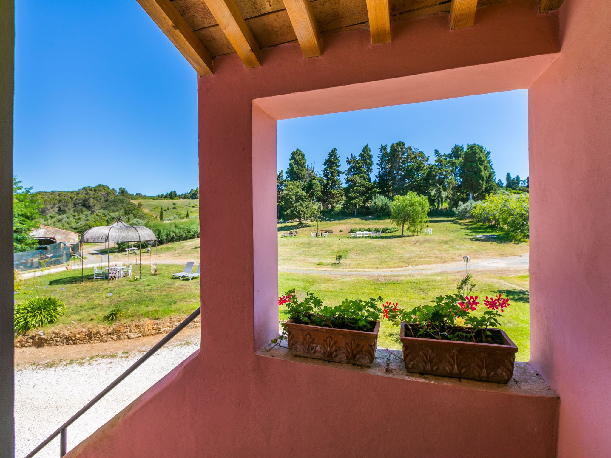 En balkon med udsigt over et grønt landskab, inklusive en sommerpavillon og plantekasser.