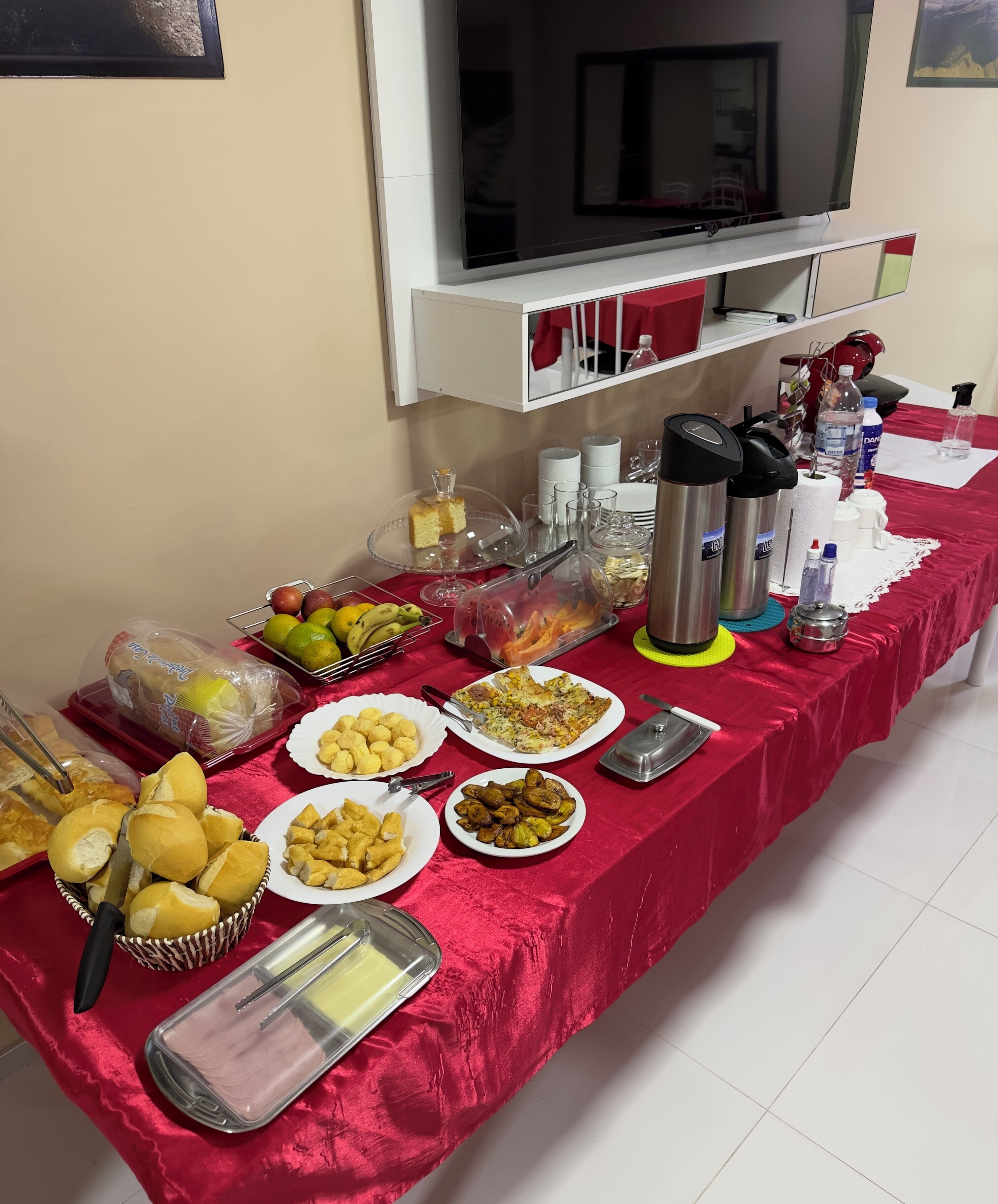 Ein Buffet mit verschiedenen Speisen und Getränken, ein an der Wand befestigter Fernseher und ein weißes Schranksystem darüber.
