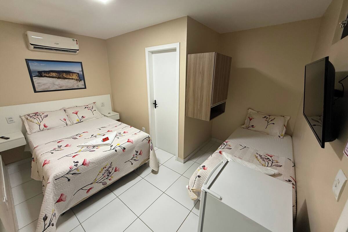 A bedroom with a bed, a desk, a chair, a wardrobe, a television, and an air conditioning unit.