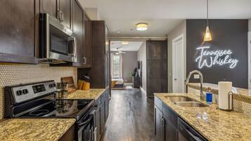 A modern kitchen with dark wood cabinets, granite countertops, stainless steel appliances, and a neon sign reading "Tennessee Whiskey".