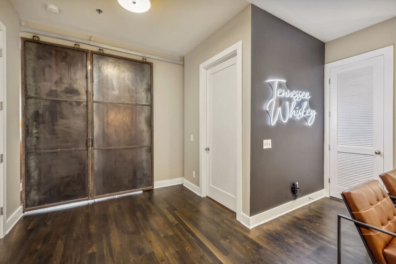 A room with a dark wood floor, a sliding door, a neon sign reading "Tennessee Whiskey", and a chair.